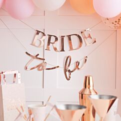 Ruusukultainen polttaribanneri tekstillä "BRIDE to be".
